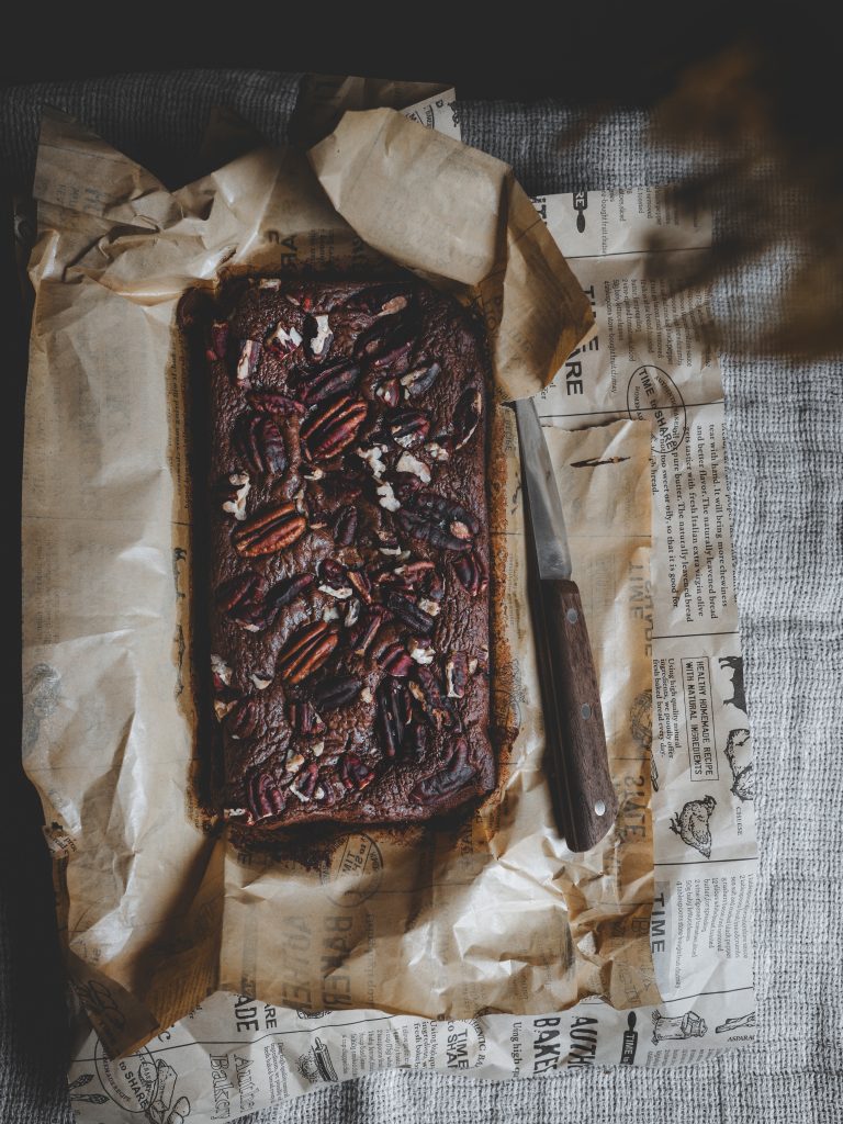Brownie al cioccolato e caffè con burro nocciola e noci pecan, appena sfornato su carta da forno stropicciata con coltello accanto.