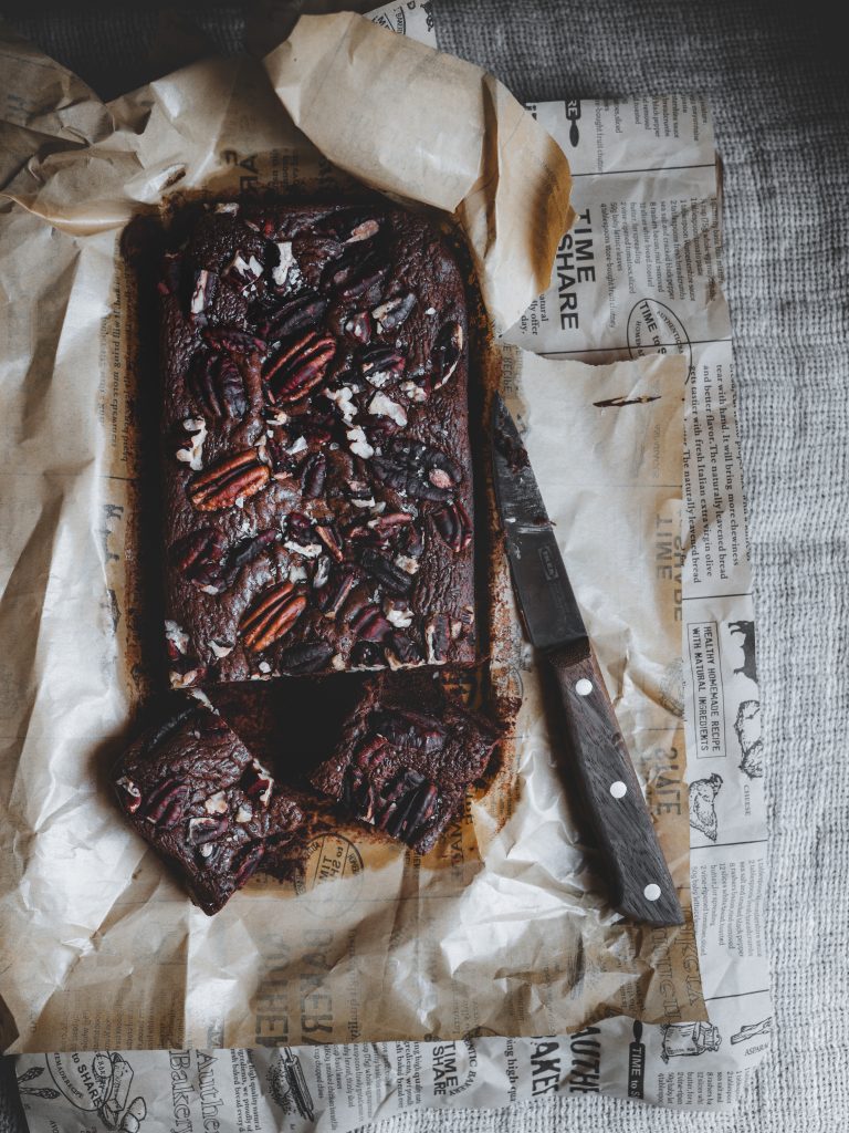 Brownie al cioccolato e caffè tagliato a quadrotti con noci pecan su carta da forno, coltello in legno accanto.