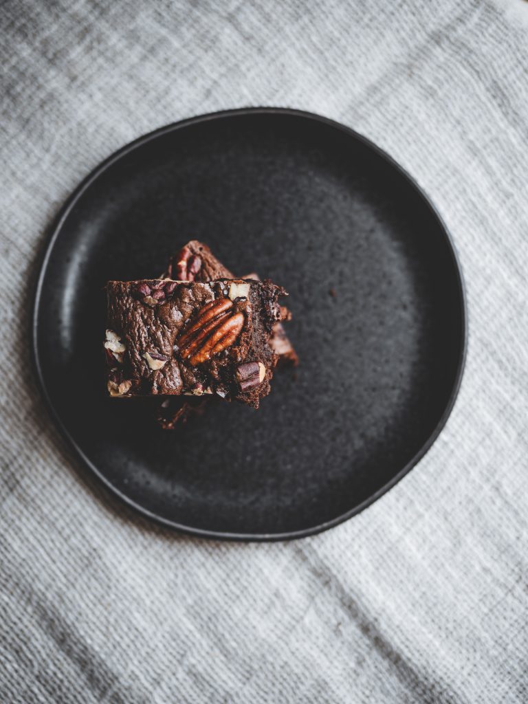 Quadrotto di brownie al cioccolato e caffè con noci pecan su piatto nero minimal.