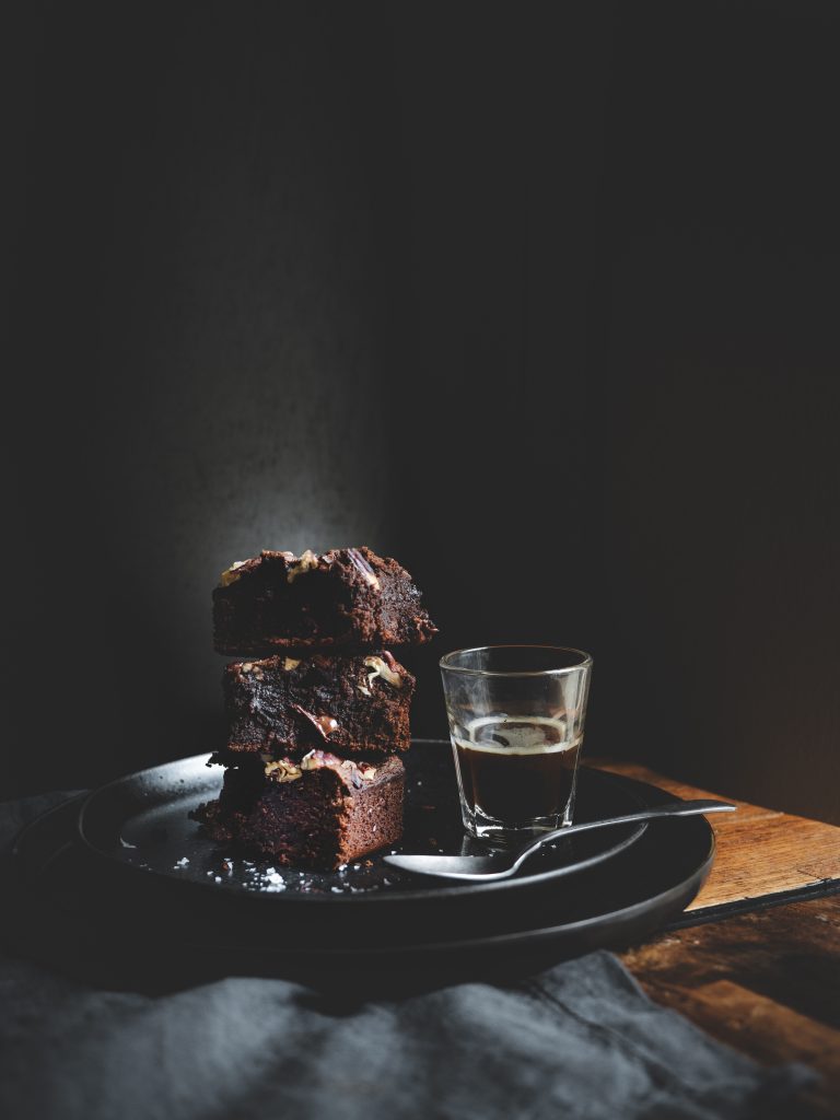 Brownie al cioccolato con noci pecan servito con espresso su piatto nero.