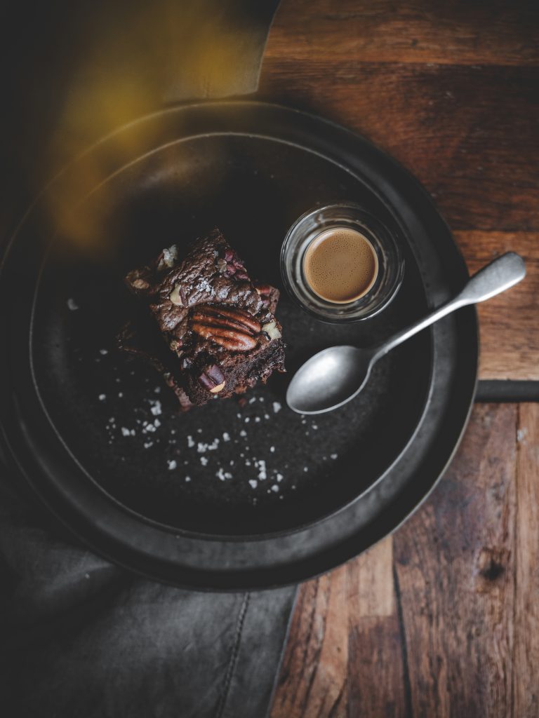 Vista dall’alto di brownie al cioccolato con pecan servito con espresso su piatto nero.