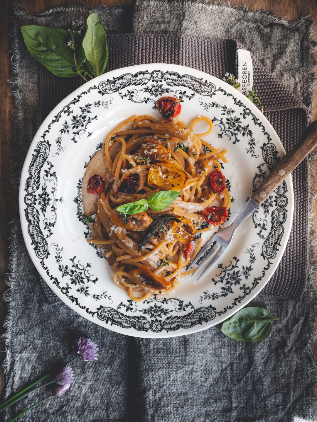Spaghetti al confit di pomodori con crema di caciocavallo e aglio nero serviti in piatto bianco.