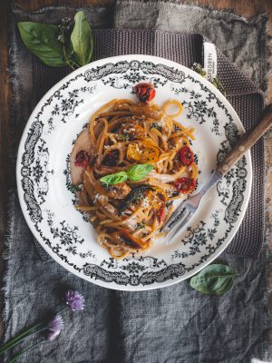 Spaghetti al confit di pomodori con crema di caciocavallo e aglio nero serviti in piatto bianco.