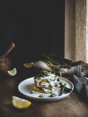 Pancake salati fave asparagi con crema di pecorino serviti a torre su tavolo rustico illuminato da luce naturale