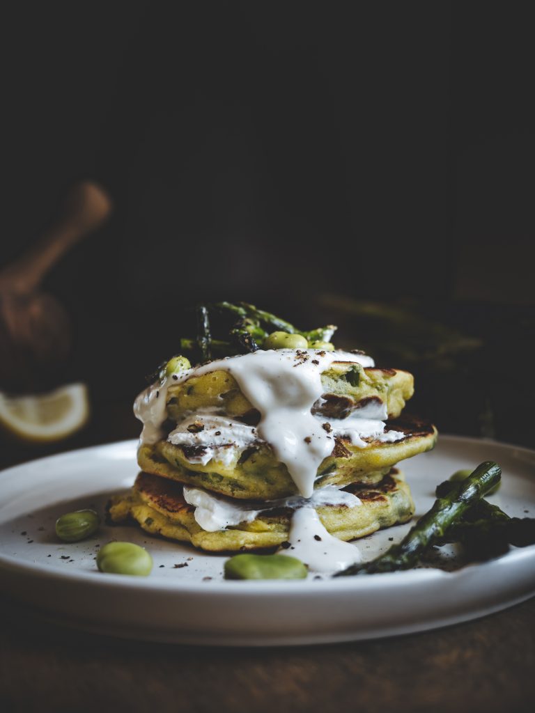 Dettaglio ravvicinato di pancake soffici con crema di pecorino colata sopra e pepe macinato.
