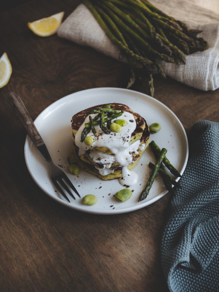Pancake di primavera su piatto bianco con limone fresco, tessuto naturale e ingredienti di scena.
