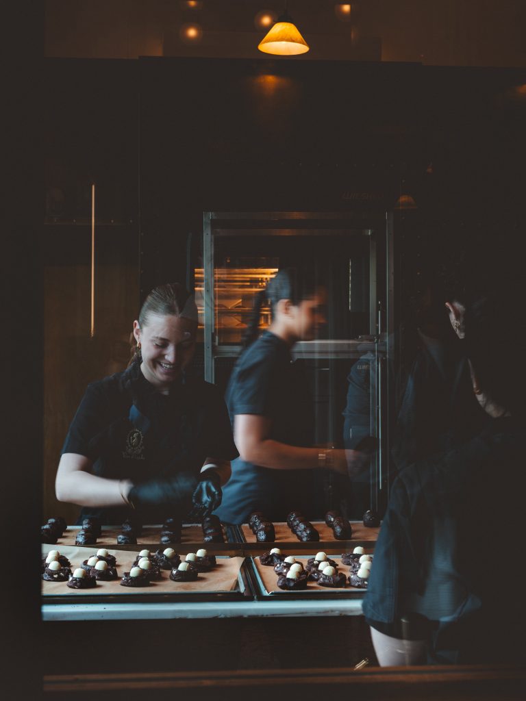 Laboratorio artigianale di dolci al cioccolato ad Amsterdam con personale al lavoro dietro il bancone.