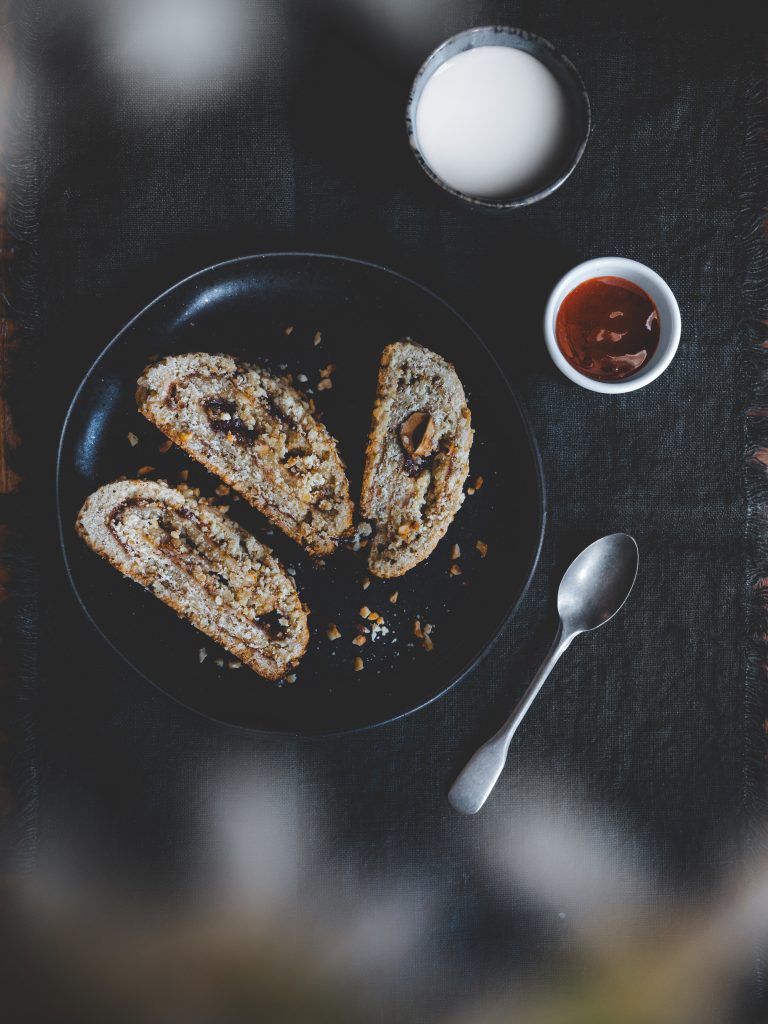 Frolla arrotolata all’avena e nocciole con confettura di prugne goccia d’oro servita su piatto nero.