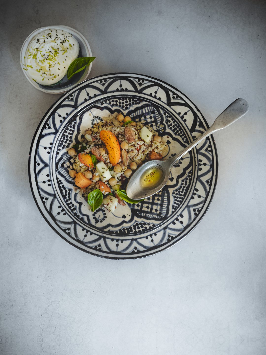 Insalata di bulgur e quinoa con barattiere, albicocche, ceci e kefir al limone servita in un piatto decorato